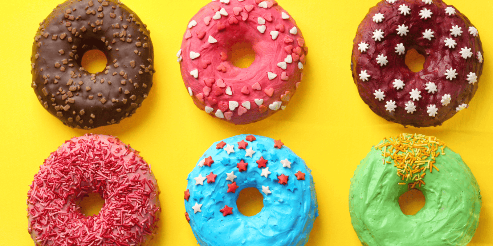 different flavoured donuts with different sprinkles laying on a yellow background