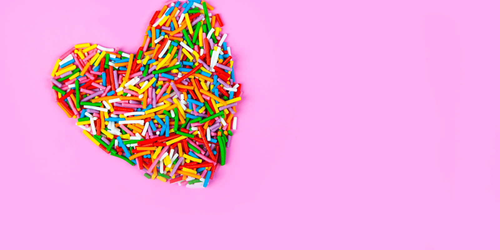 multi coloured sprinkles shaped as a heart on pink background