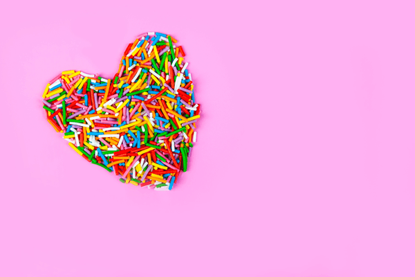 multi coloured sprinkles shaped as a heart on pink background